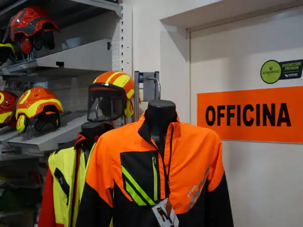 Manichino con abbigliamento antitaglio STIHL e caschi forestali KASK accanto all'insegna Officina