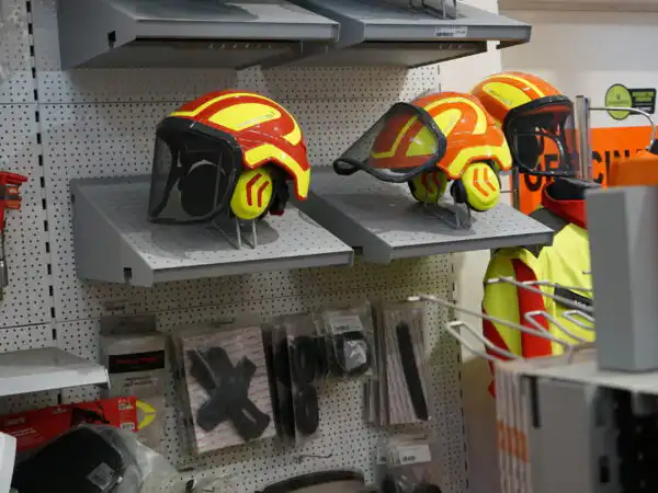 Espositore di caschi da lavoro forestale con visiera e cuffie antirumore su mensole
