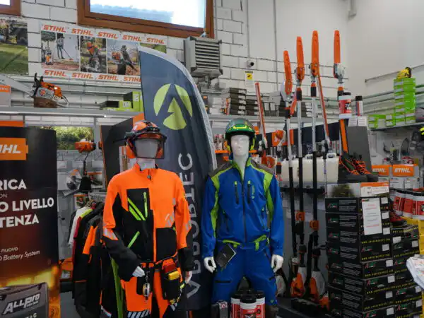 Due manichini con casco e abbigliamento protettivo STIHL, espositore attrezzi da giardino