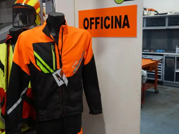 Manichino con completo antitaglio STIHL arancione e giallo accanto al cartello Officina